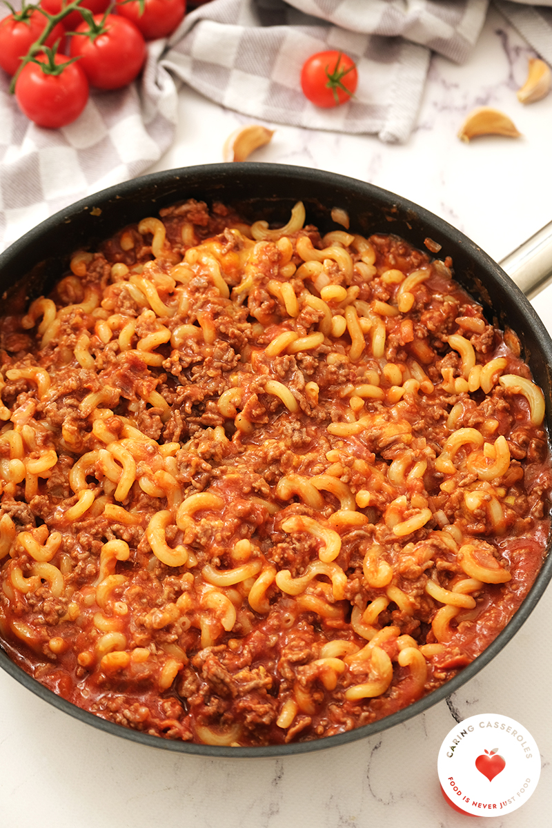 meat sauce mixed with cooked pasta in skillet