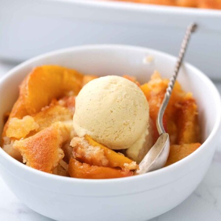 peach cobbler dessert recipe in white bowl topped with ice cream