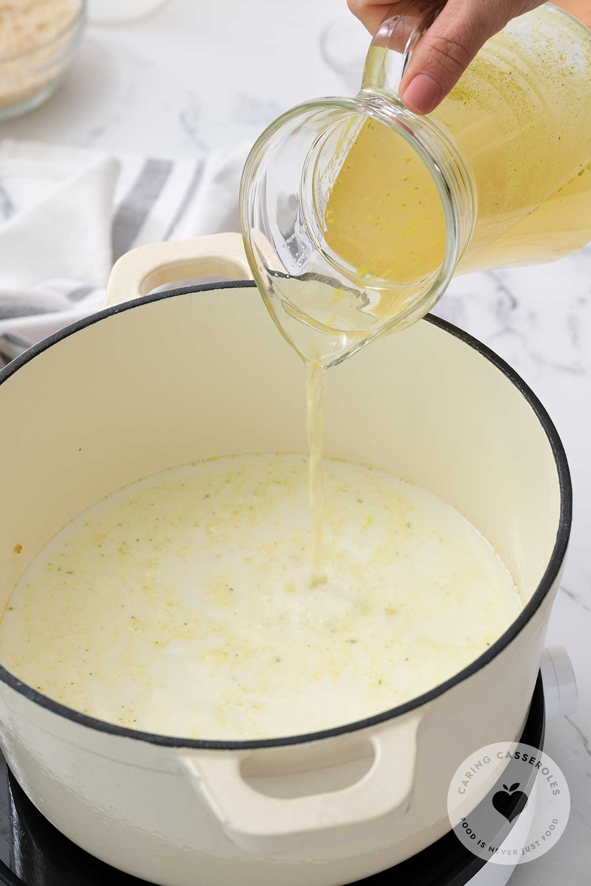 After adding flour to make a roux, chicken stock and milk is slowly added and whisked in the pot.
