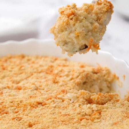 chicken and rice casserole in white serving dish with spoon taking scoop of the rich and creamy casserole out