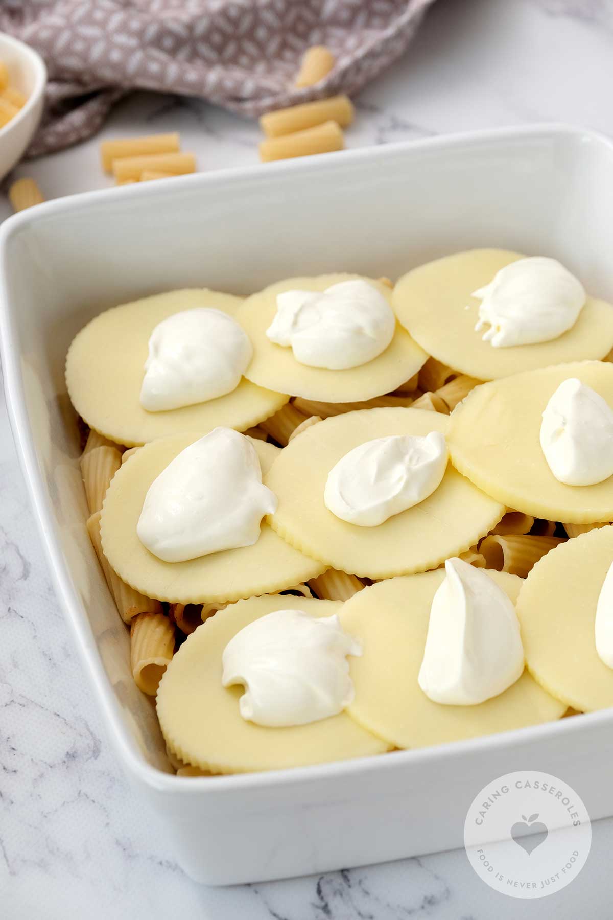 Ground beef mixture and pasta added to a baking dish and topped with provalone discs.
