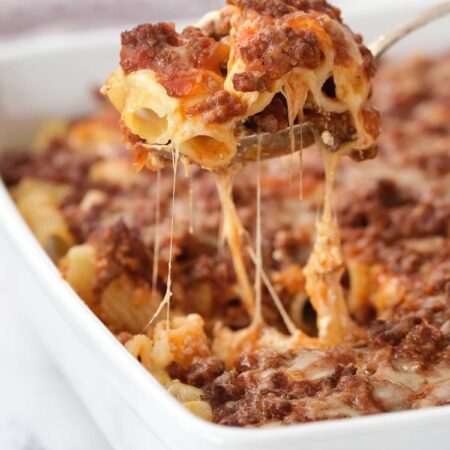 Penne pasta casserole being served from a large white dish.