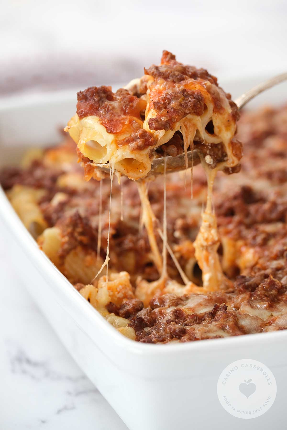Penne pasta casserole being served from a large white dish.