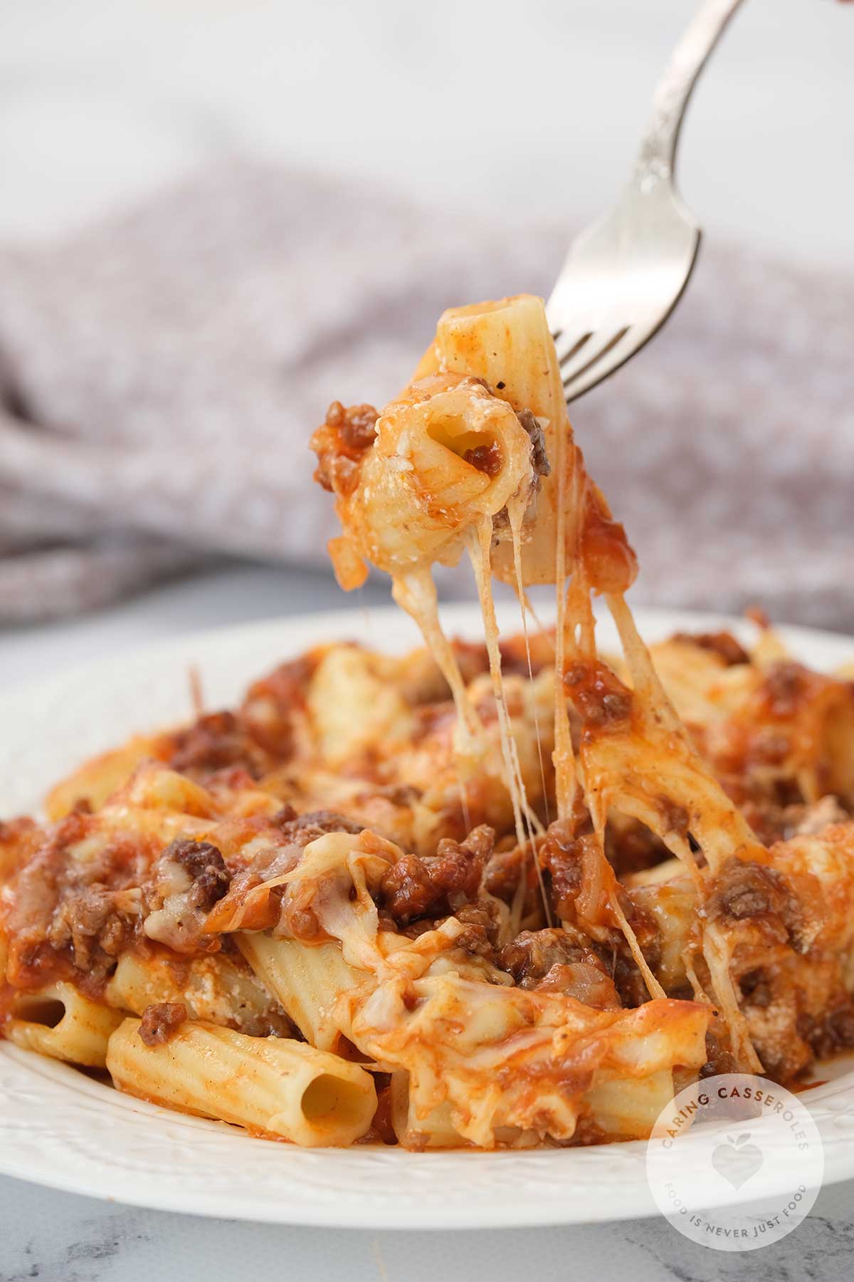 Hot baked penne pasta with sausage in a casserole dish, golden and bubbling with melted cheese on a white plate