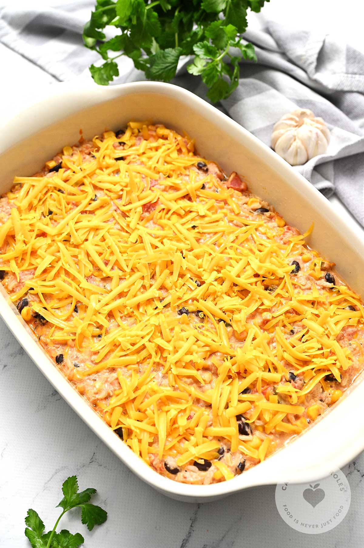 Mixture placed in a baking dish and topped with cheddar cheese, ready to bake in the oven.