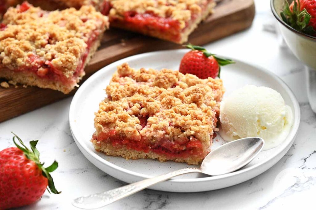 Strawbeery Crumb Bars served on a white place with ice cream made from a recipe from Caring Casseroles.