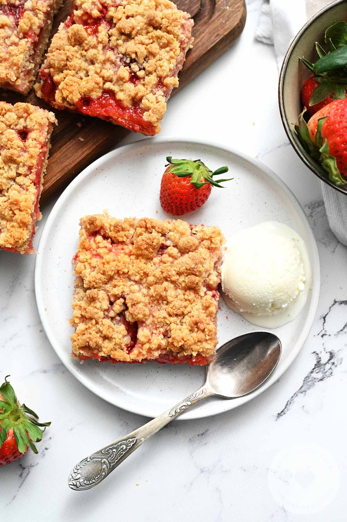Ice cream and strawberry crumb bars served on a white plate.