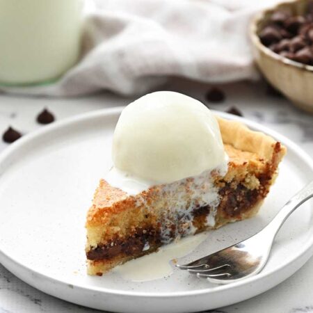 A piece of chocolate chip cookie pie on a white plate with a fork.