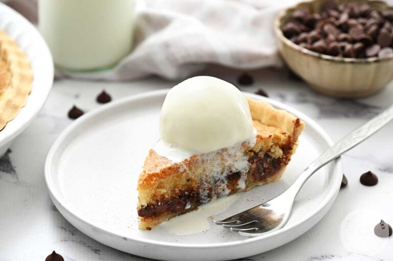 A piece of chocolate chip cookie pie on a white plate with a fork.