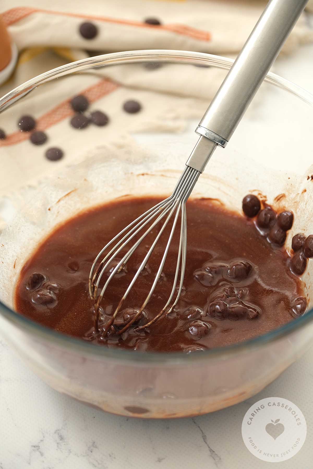 Chocolate melting in a bowl while being stirred with a whisk.