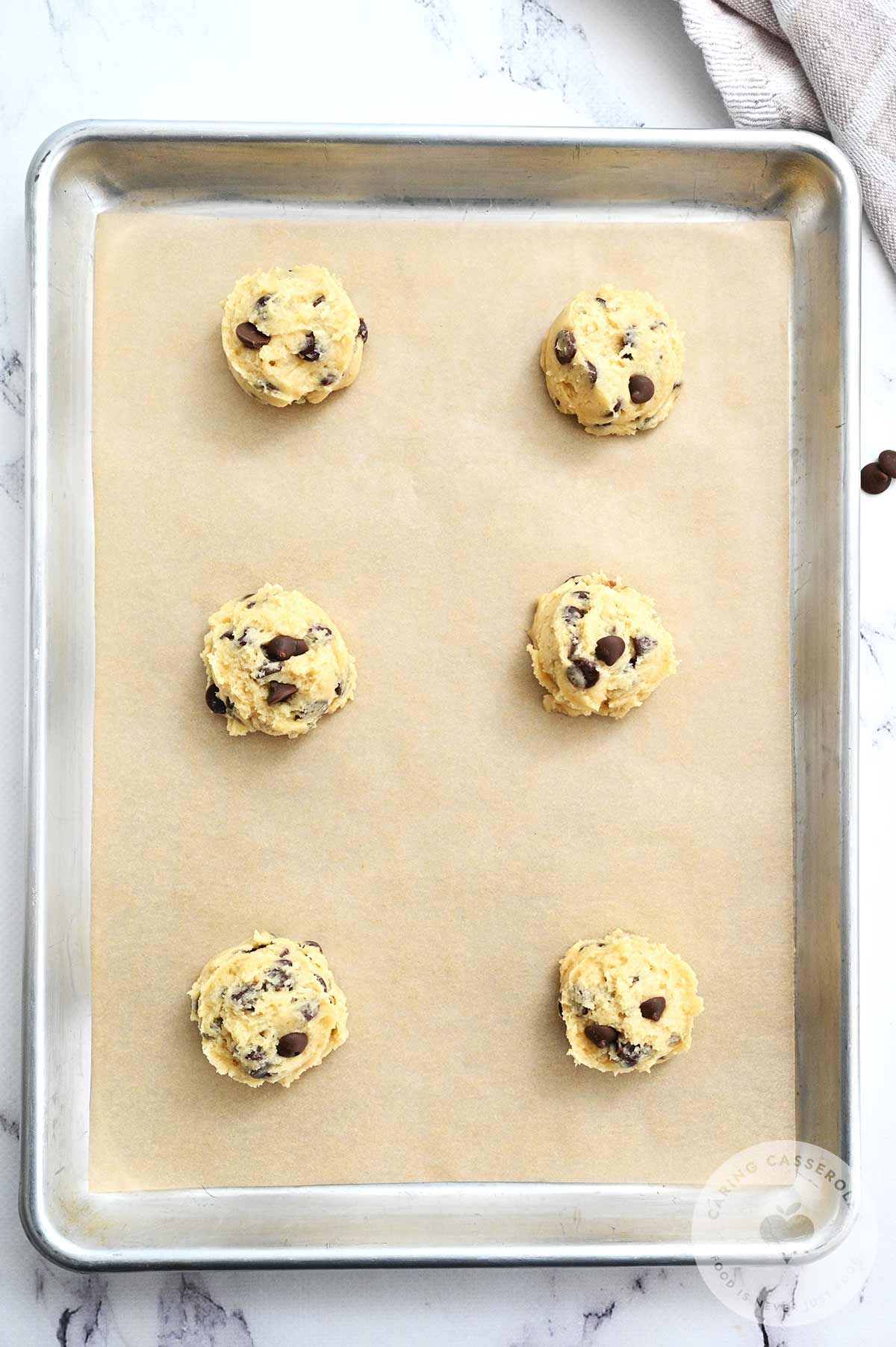 Cookie dough balls scoped onto backing paper on a baking tray.
