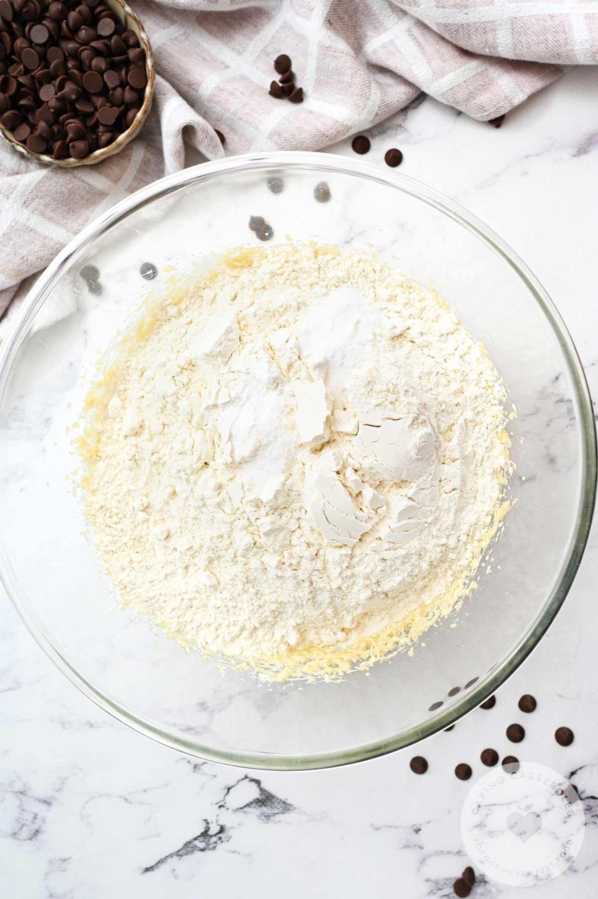 Flour added to the butter, sugar and egg mixture in a bowl.