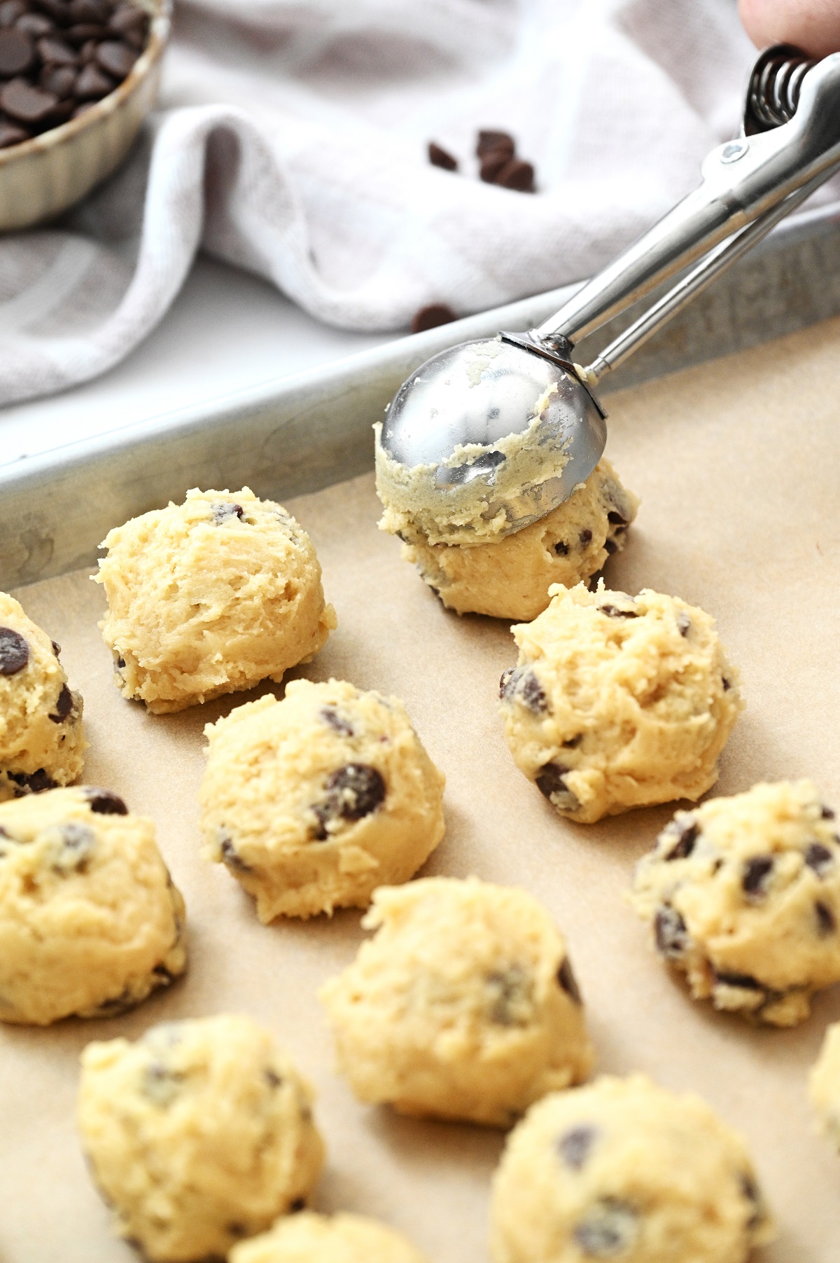 Cookie dough scooped up with a cookie scoop and placed on a baking sheet lined with parchment paper.